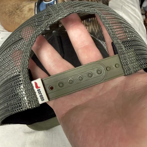 Reviewer's hand holding the back of the Big Flat Bill Structured Mesh Hat, showing the adjustable green snapback.