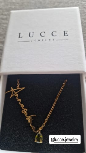 Customer's gold Lucce Signature Necklace with name script and teardrop-cut stone, sitting inside its branded jewelry box.