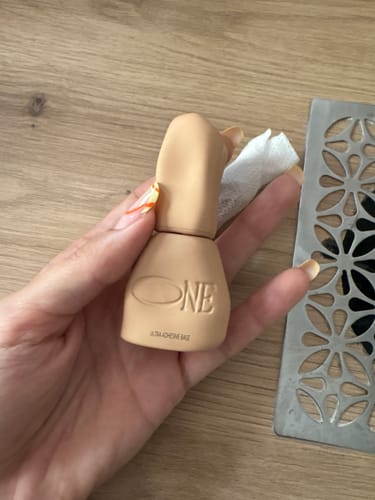 Customer's hand holding a beige Ultra Adhesive Base bottle with a modern design