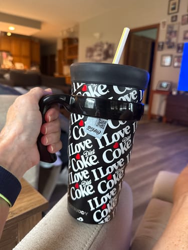 Customer's hand holding a black To-Go Buddy handle attached to a black patterned Diet Coke tumbler.