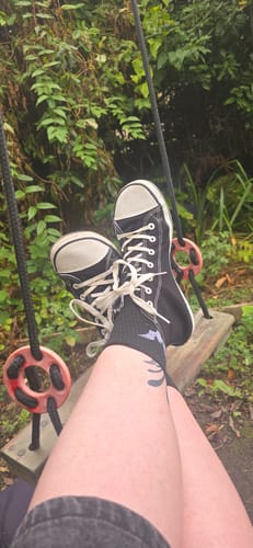 Customer's feet wearing black and white Roam I barefoot shoes while resting on a backyard swing.