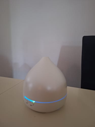 Customer's Unity 2.0 diffuser in warm grey placed on a table, emitting a soft blue light