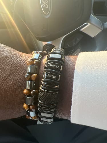 Customer's black personalized bracelet worn on wrist next to a beaded bracelet while in a car.