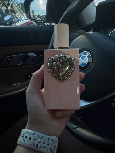 Customer's hand holding the D&G My Devotion Intense perfume bottle, featuring a heart emblem, inside a car.