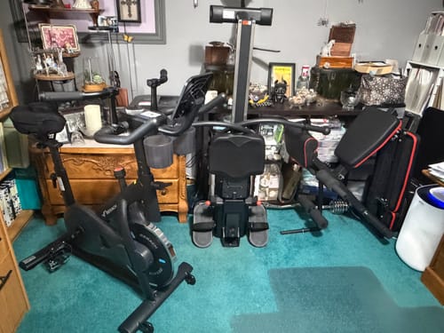 Customer's NovaRow RS3 rowing machine, black exercise bike, and weight bench set up in a home office.