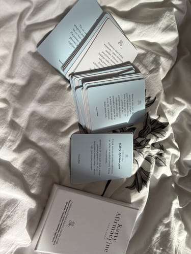Customer's Karty Afirmacyjne cards in light blue lying on a wrinkled white bedsheet.