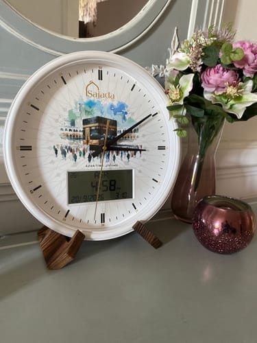 Reviewer's Sajada Azan Clock featuring a Holy Kaaba illustration, resting on a wooden stand next to a floral vase.