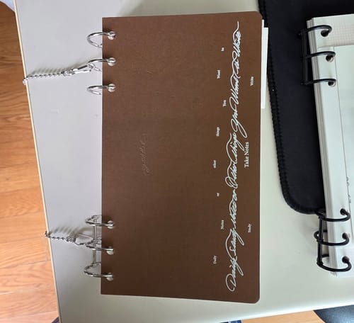 Customer's brown Index Notebook 3.0 with white printed text, attached to a metal lanyard system on a light surface.