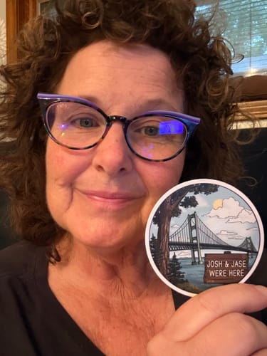 Customer's hand holding a circular Josh and Jase Mail Club sticker featuring an illustration of a bridge.