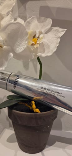 Customer's Le baume nettoyant tube posé dans un pot à fleurs devant une orchidée blanche.