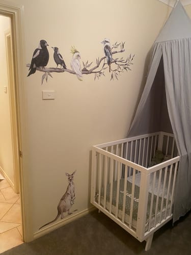 Customer's Extended Gum Tree Branch + Animals decal showing birds and a kangaroo on a nursery wall near a crib.