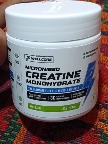 Customer's white tub of Wellcore Micronised Creatine Monohydrate in Kiwi Kick flavor, sitting on a textured surface.