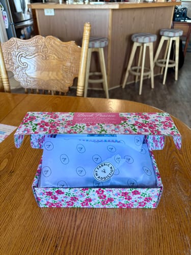 Customer's Brick Prairie Precut Quilt Kit box resting on a wooden table, featuring floral print packaging.