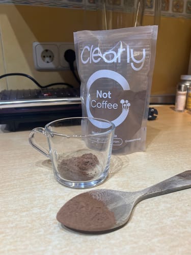 Customer's Not Coffee pouch with a glass cup and wooden spoon containing brown powder on a kitchen counter.