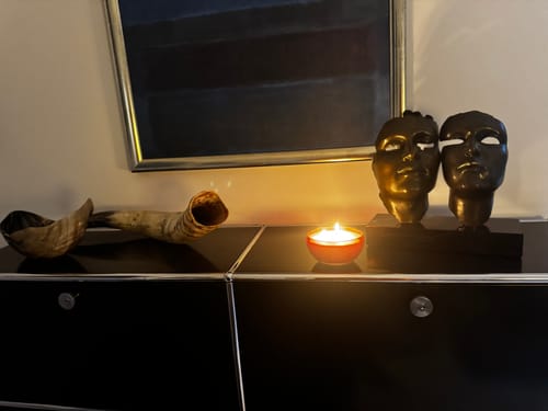 Customer's Yazd Duftkerze burning with a warm glow on a dark sideboard next to decorative sculptures.