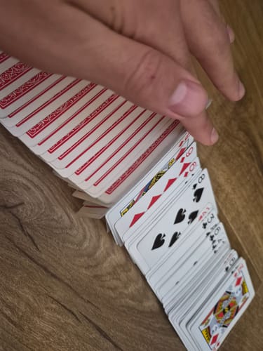 Reviewer's hand fanning out a deck of red Bicycle Playing Cards on a wooden surface.