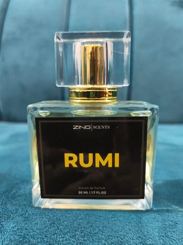 Customer's Rumi perfume bottle in a square glass design with gold details, set against a teal background.