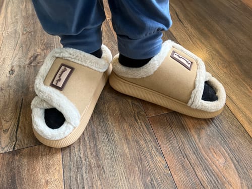 Kunds bekväma, beige HappyFluff-tofflor med vitt mjukt foder på ett trägolv.