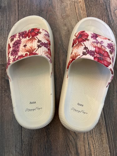 Customer's ljusa HappyFlops Botanics tofflor med blommotiv, stående på ett trägolv.