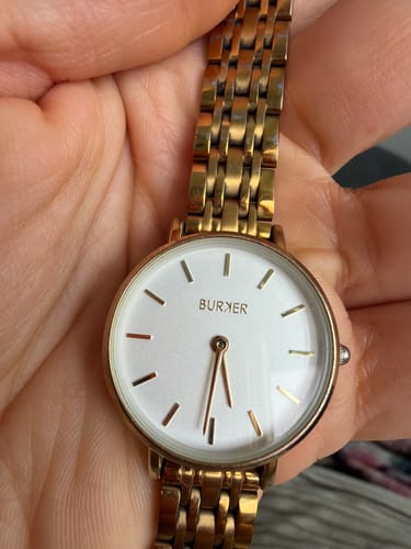 Customer's Isabell Petite Gold Brown watch, featuring a round white face and gold link band held in a hand.