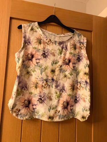 Customer's Garden Delight Linen Viscose Fabric fashioned into a sleeveless top hanging on a door.