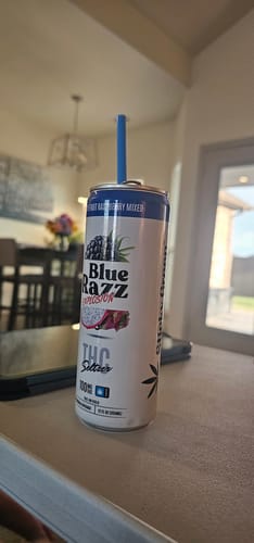 Customer's Blue Razz Explosion THC Infused Soda can with a blue straw on a table.