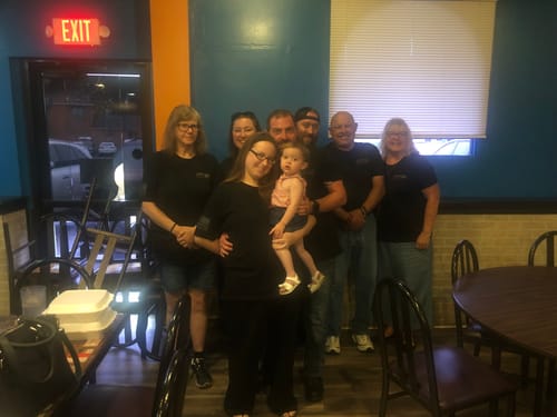 Customer's group of adults and one child posing while wearing black 9/11 Never Forget shirts in an indoor setting.