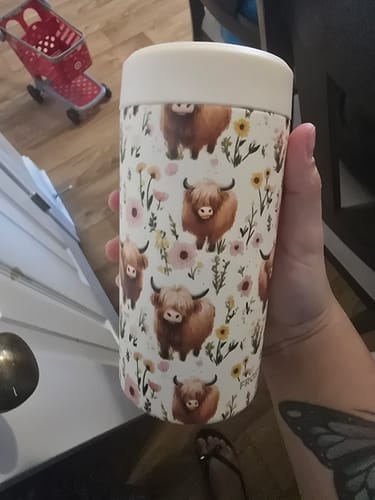 Customer's Universal Buddy Highland Cow cooler held in hand with a cream lid against a home background