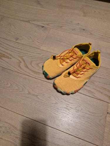 Kundenfoto der gelben Smart II Barfußschuhe mit orangen Schnürsenkeln auf einem hellen Holzboden.