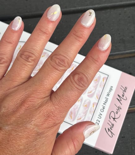 Kundenhand mit aufgetragenen Gold Rush Marble UV Gel Nail Wraps, die auf der Produktverpackung liegt.