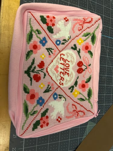 Customer's completed Love Letters Needlepoint Pouch Kit featuring floral, dove, and heart motifs in pink.