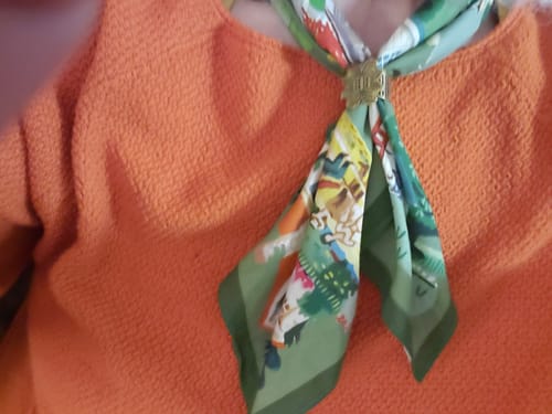 Customer's Suburbs Bandana with olive green details and illustrated homes, styled with a scarf ring over an orange shirt.