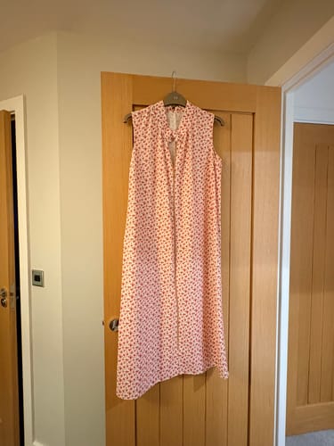 Customer's summer dress made from ditsy pink floral linen mix fabric, hanging on a door.