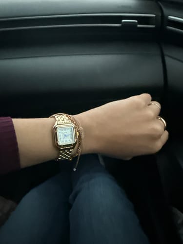 Customer's gold Grealy De Mains watch worn on the wrist, paired with a delicate bracelet in a car interior.