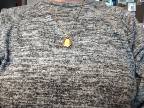 Customer's personalisierte Fingerabdruck Halskette als goldfarbene Kette mit rundem Anhänger an einem grauen Pullover