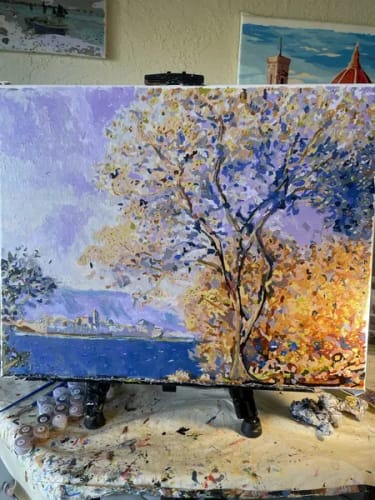 Customer's Custom Paint By Numbers landscape on an easel, featuring an impressionist tree, water, and distant buildings.