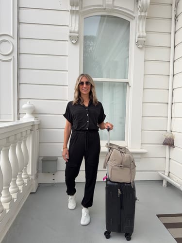 Reviewer's black Brigitte Brianna Cargo Jumper worn with white sneakers and travel luggage on a white porch.