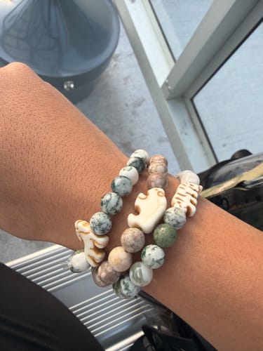 Customer's wrist wearing a stack of colorful beaded Roam Bracelets with animal-shaped charms.