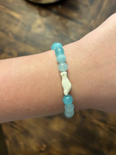 Customer's Glide Bracelet featuring blue beads and a white seal charm worn on their wrist.