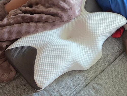Customer's white ergonomic memory foam pillow with textured pattern resting on a sofa under a brown blanket.