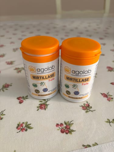 Customer's two white bottles of Agolab Mirtillase Forte supplements with orange lids standing on a floral tablecloth