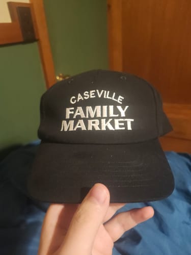 Customer's Big Relaxed Cap held in hand, showing black fabric and white Caseville Family Market embroidery.
