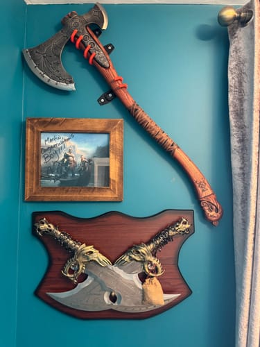 Customer's hand-forged Leviathan axe mounted on a teal wall alongside a framed picture and crossed wall-mounted swords