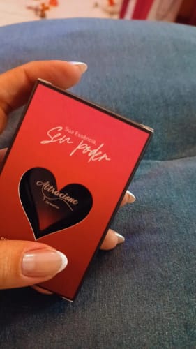 Customer's hand holding the red rectangular box of the Attracione Sensual perfume with a heart-shaped cutout.