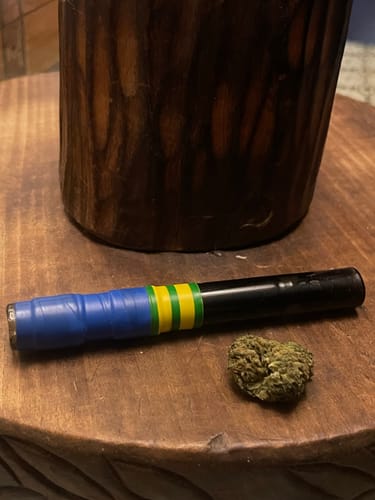 Reviewer's green, textured cannabis bud next to a blue, green, and black smoking accessory on a wooden table.