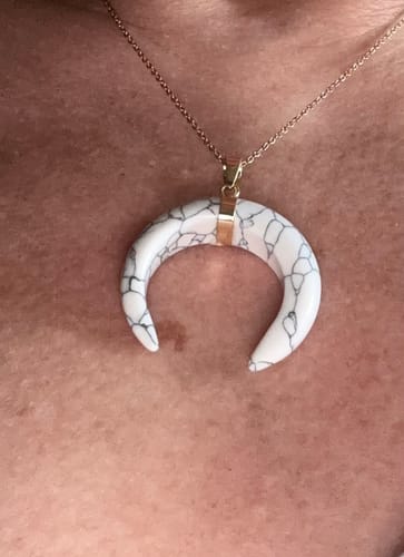 Customer's white crescent-shaped Howlite pendant with dark veining, worn on a gold chain against skin.