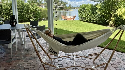 Customer's Go Hammock set up on a patio, with a person reclining in the white hammock on a steel frame.