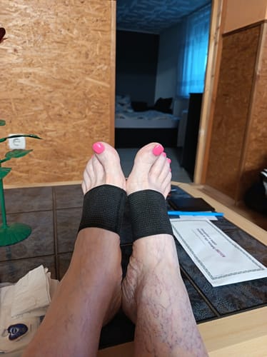 Reviewer's feet wearing black, textured copper infused arch support bands while resting.
