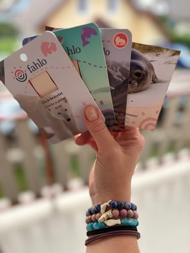 Customer's hand wearing multiple Glide Bracelets, holding cards showing different animals.