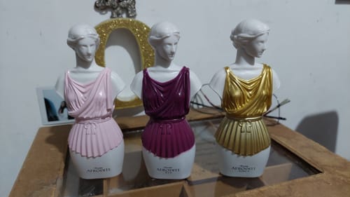 Customer's Kit Afrodite set of three female bust perfume bottles in pink, purple, and gold on a table.